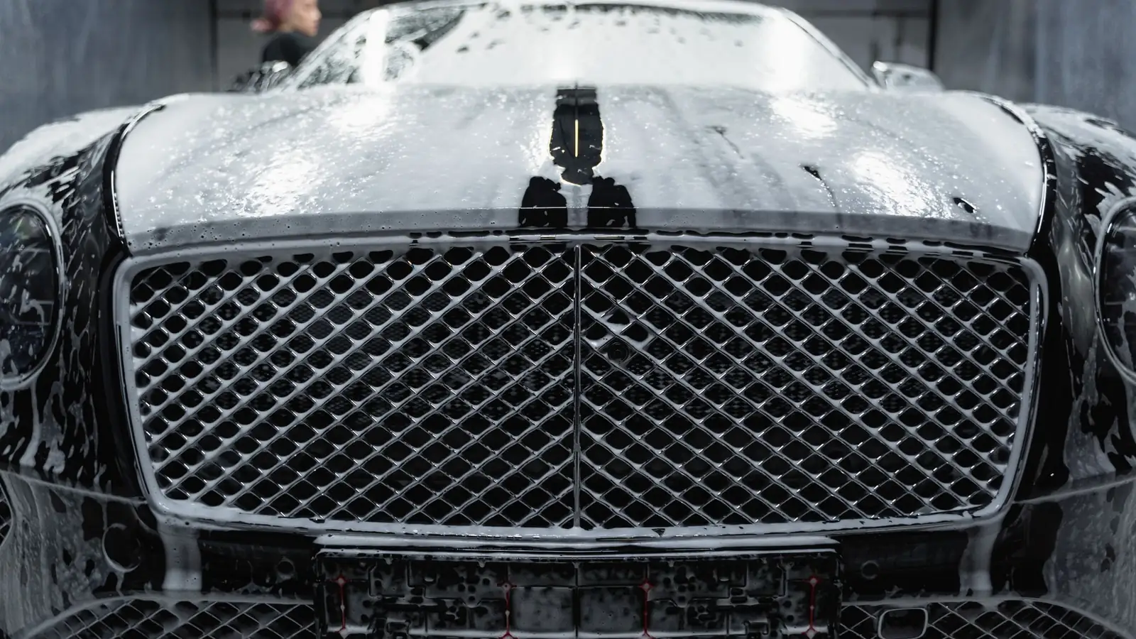 Frente de un auto negro cubierto de espuma de lavado